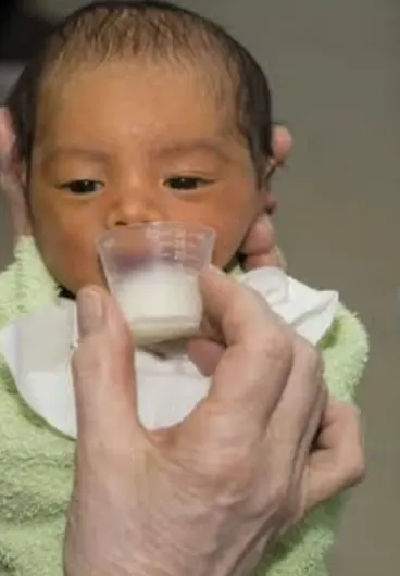 Bebé recibiendo leche con un vasito
