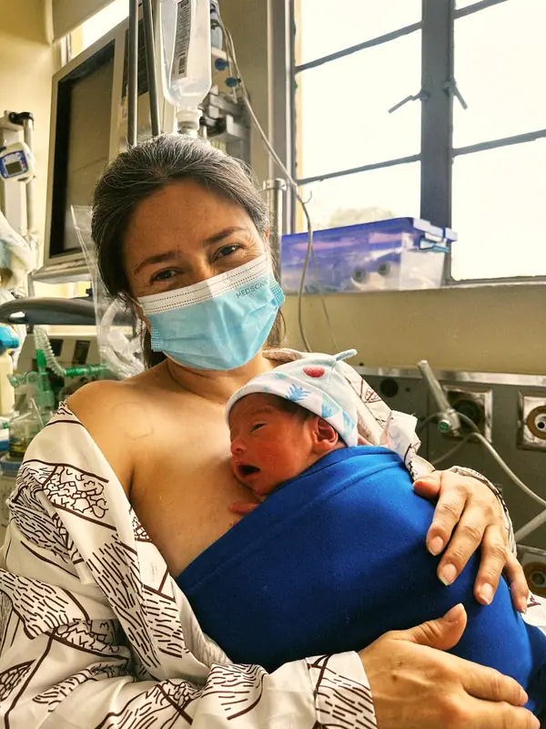 Adulto con tapabocas cargando a un bebé dentro de una faja azul
