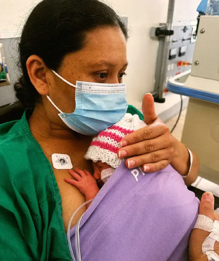 Mamá con tapabocas sosteniendo a su bebé con gorro de colores