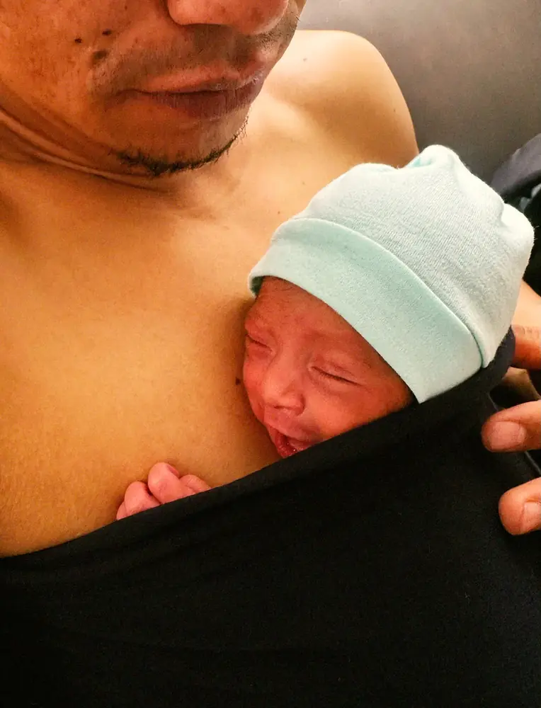 Bebé con gorro, piel con piel sobre el pecho de un adulto