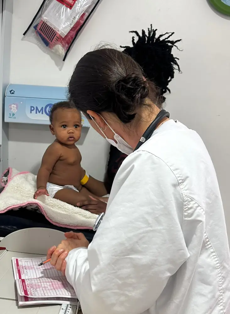 Profesional de salud con tapabocas valorando a un bebé en consulta